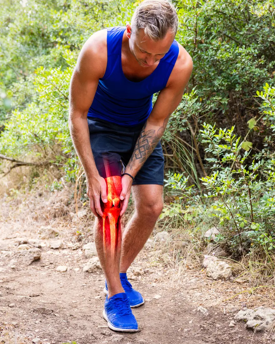 A hiker stopping on a trail to hold his knee, the joint highlighted