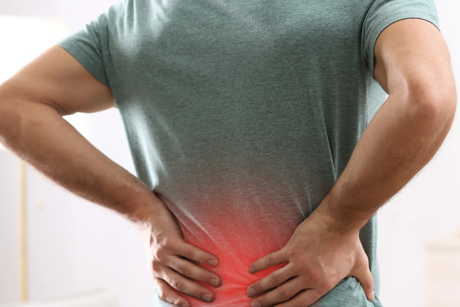 A man standing with both hands at his lower back